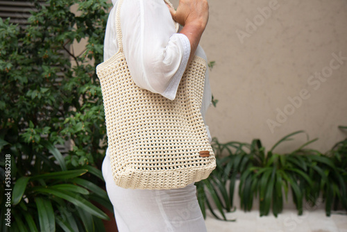 Woman holds a handmade beige knitted bag in her hand outdoors. Sustainable shopping. Wasteless lifestyle. Female with a jute bag with her own hands on a walk