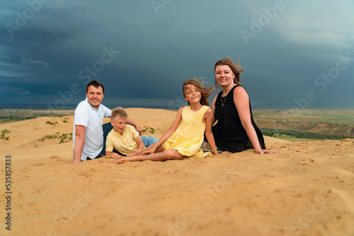 Happy family of mother, father, daughter and son having fun on sand dunes on vacations together. Happy family of four sitting on high sand dune at mountains. Fun happy lifestyle in summer