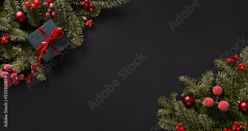 Christmas winter banner with fir branches, red balls on black background. Xmas greeting card. Holiday time. Happy New Year. Space for text. View from above, flat lay.