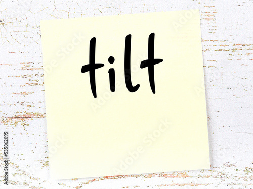 Yellow sticky note on wooden wall with handwritten word tilt