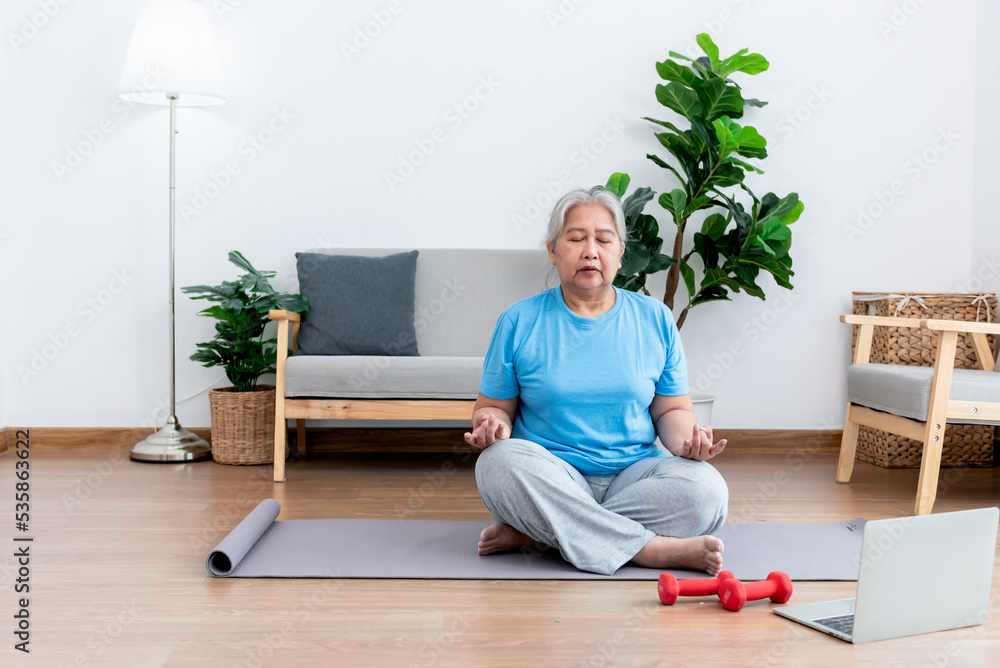 Asian elderly women is practicing yoga in the basic position in her living room, which is a warm-up and meditation exercise, to elderly health care concept. Asian elderly women is practicing yoga in the basic position in her living room, which is a warm-up and meditation exercise, to elderly health care concept.