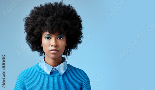 Portrait of black woman, fashion afro and serious face with an expression of focus on blue background studio mockup. Trendy earing accessory, stylish cool clothing and blue cosmetic eyeshadow makeup photo