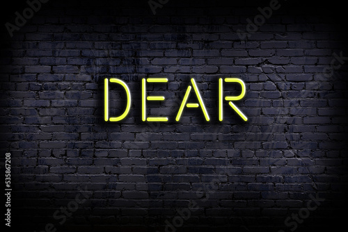 Neon sign. Word dear against brick wall. Night view