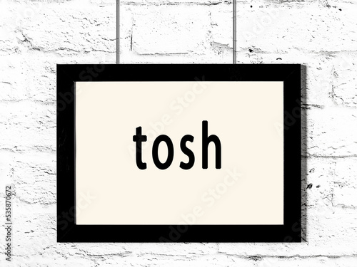 Black frame hanging on white brick wall with inscription tosh photo