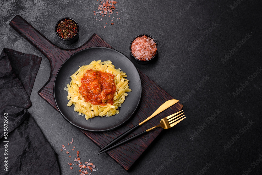 Pasta with beef meatballs in tomato sauce with spices and herbs on a dark background