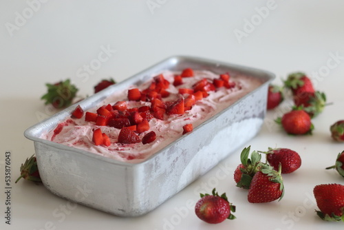 Homemade strawberry ice cream taken out from freezer in a loaf tin served with strawberry slices on top