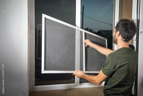 Man installing the mosquito net on the window.