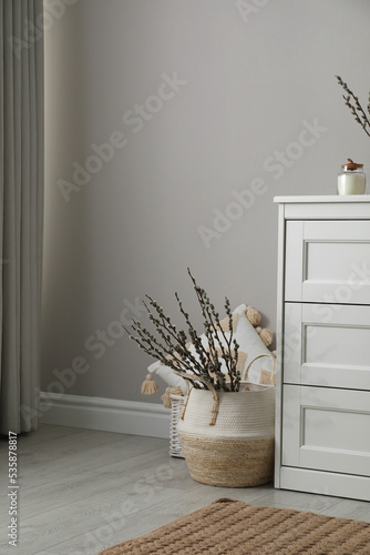 фотографія Basket with pussy willow branches near chest of drawers indoors