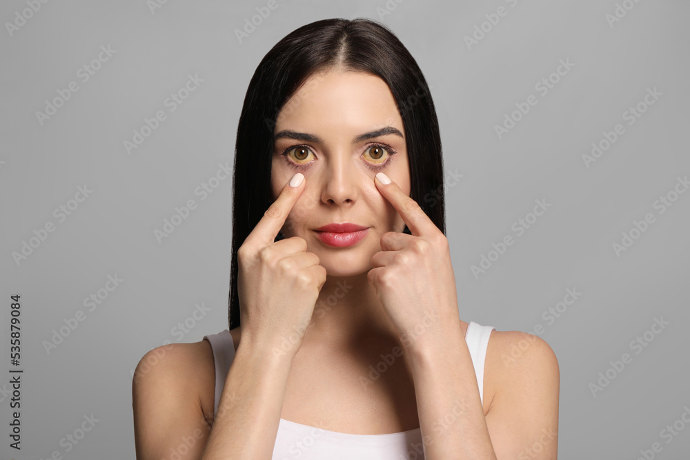 Woman checking her health condition on grey background. Yellow eyes as symptom of problems with liver Woman checking her health condition on grey background. Yellow eyes as symptom of problems with liver
