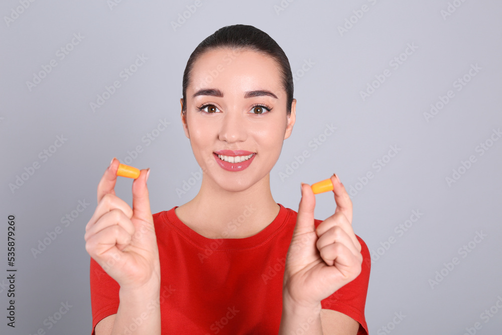 Young woman with foam ear plugs on grey background Young woman with foam ear plugs on grey background