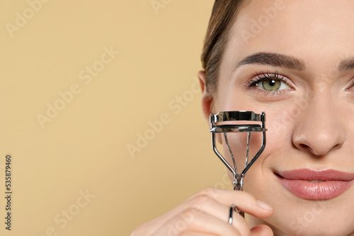 Woman with eyelash curler on beige background, closeup. Space for text