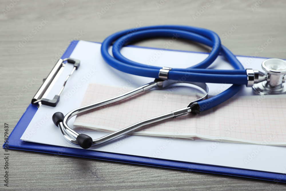 Clipboard with stethoscope and cardiogram on wooden table, closeup Clipboard with stethoscope and cardiogram on wooden table, closeup