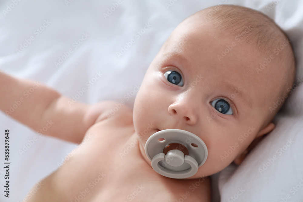 Cute little baby with pacifier lying on bed, closeup Cute little baby with pacifier lying on bed, closeup