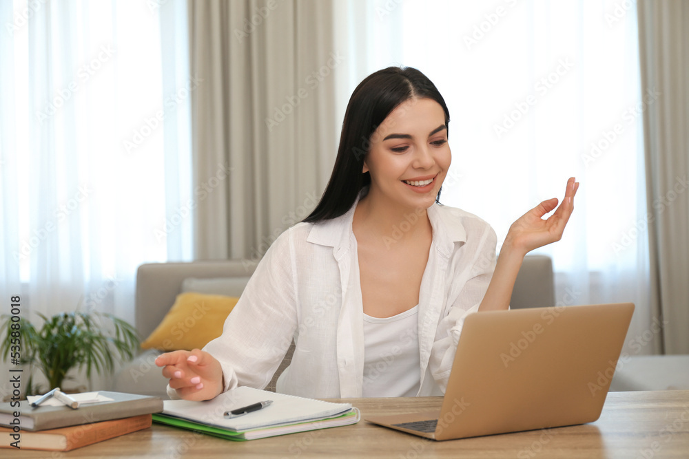 Young woman watching online webinar at table indoors Young woman watching online webinar at table indoors