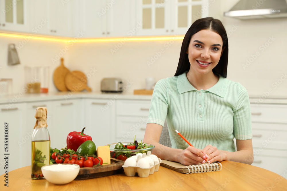 Happy woman writing in notebook near products at table. Keto diet