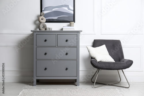Stylish room interior with grey chest of drawers and comfortable chair © New Africa