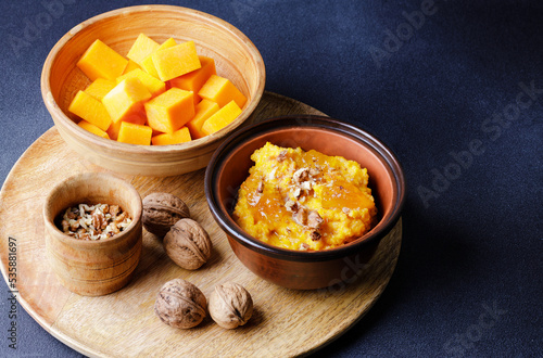 Sweet pumpkin porridge in clay bowl with jam and nuts and raw pumpkin cubes