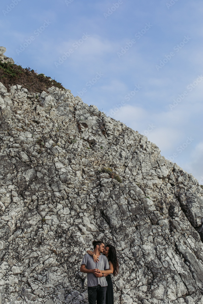 brunette woman hugging bearded boyfriend while holding hands near rocks.