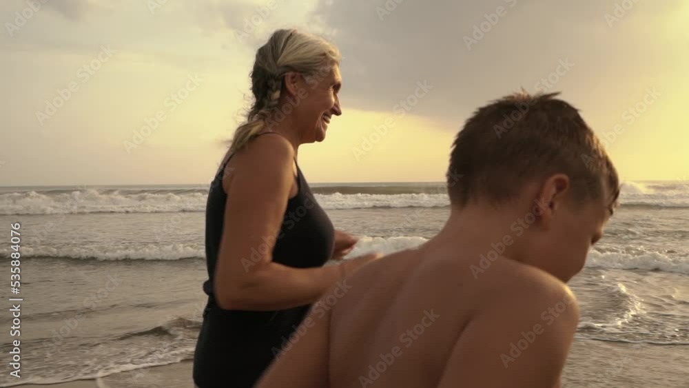 Grandmother and grandson jogging on the beach at sunset. Happy family have fun and actively spend leisure time on vacation. Grandmother and grandson jogging on the beach at sunset. Happy family have fun and actively spend leisure time on vacation.