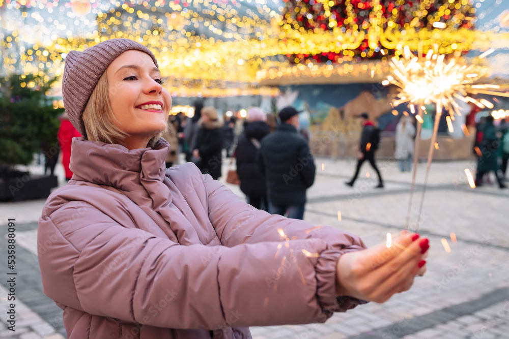 Fototapeta premium Happy girl with Christmas sparklers enjoying Christmas on the city street