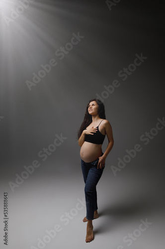 pregnant woman in studio on grey background with rays of light