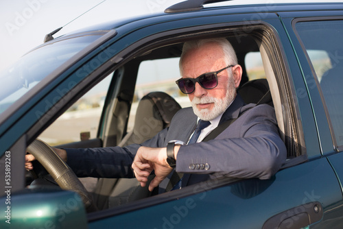 Obraz na plátne Senior businessman driving car and looking at his wristwatch while stuck in traf