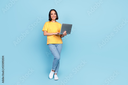 Full lenght photo of adorable young girl japanese entrepreneur hold netbook wear trendy yellow clothes isolated on blue color background