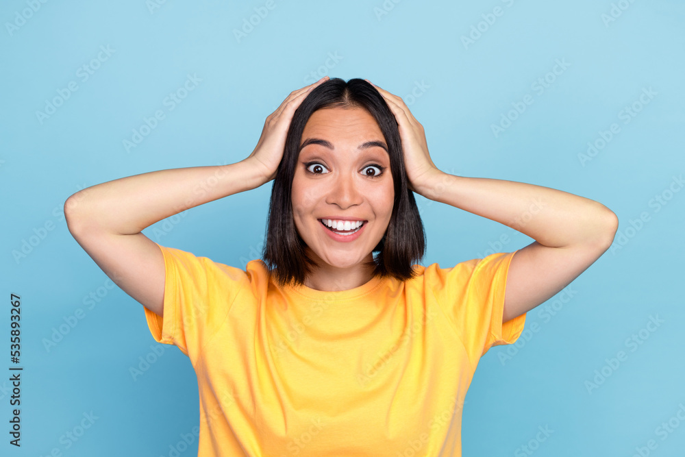 Photo portrait of pretty young lady japanese arms touch head cant believe luck wear trendy yellow look isolated on blue color background