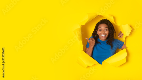 Black Woman Pointing Thumb Posing In Torn Yellow Paper © Prostock-studio