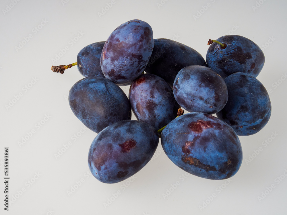 Black plums on wood background. Pile of black plums on a white serving plate. close up