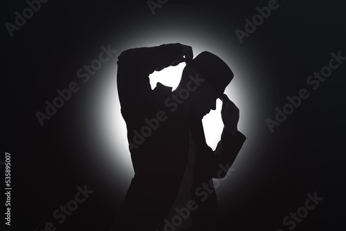 A young man adjusts his hat on his head. Bright light source in the background
