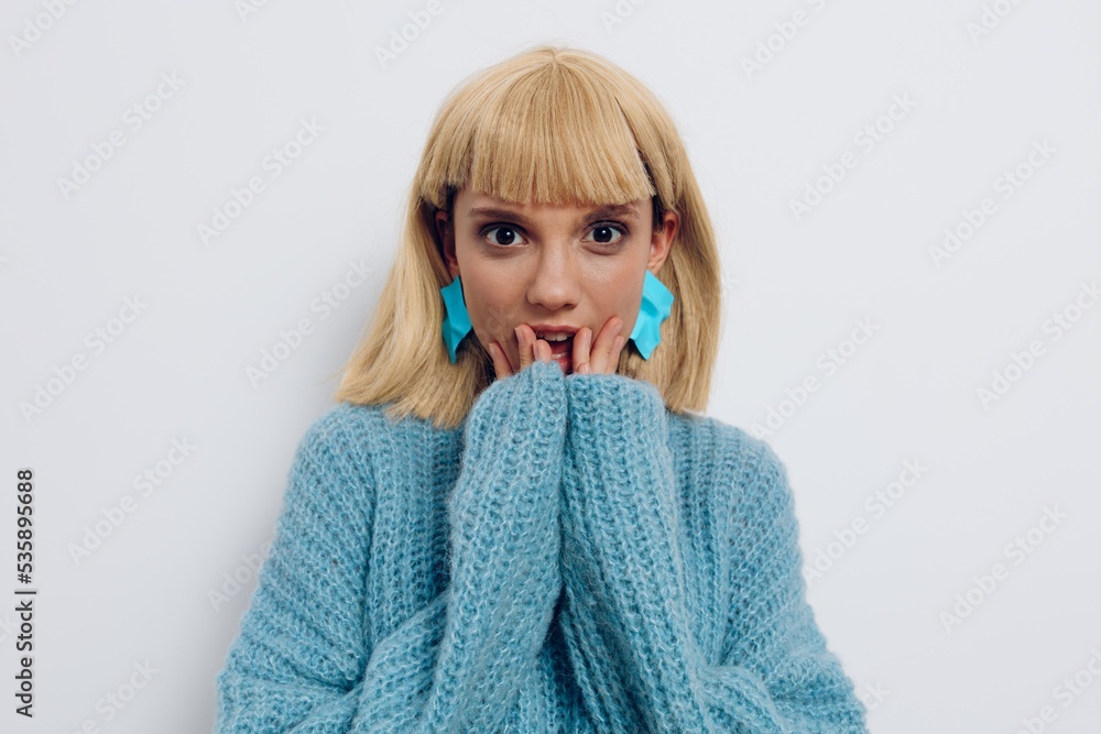 a close horizontal photo of a beautiful, sweet, pleasant woman in a stylish light blue sweater, smiling happily standing on a light background and holding her hands near her face a close horizontal photo of a beautiful, sweet, pleasant woman in a stylish light blue sweater, smiling happily standing on a light background and holding her hands near her face