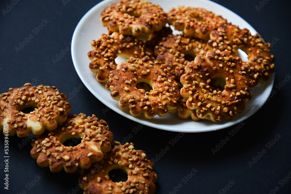 Delicious cookies with nuts on a white plate on a black background. Delicious breakfast of sweet cookies. Delicious cookies with nuts on a white plate on a black background. Delicious breakfast of sweet cookies.