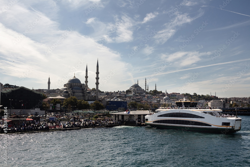 View of a ferry boat, historical mosques in Eminonu area and many people in Istanbul. It is a sunny summer day.