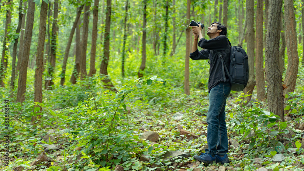 Young photographer standing in the nature, taking picture with professional camera