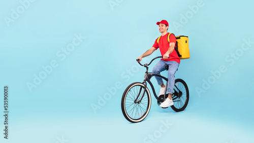 Courier Man With Backpack Riding Bike Delivering Food, Blue Background © Prostock-studio
