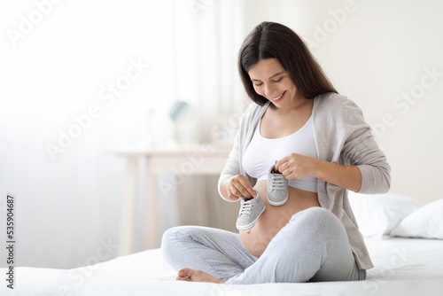 Pretty pregnant woman holding baby shoes on her big belly