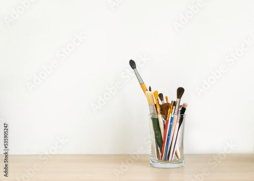 a lot of artists' brushes in a glass jar on the studio table on a white background