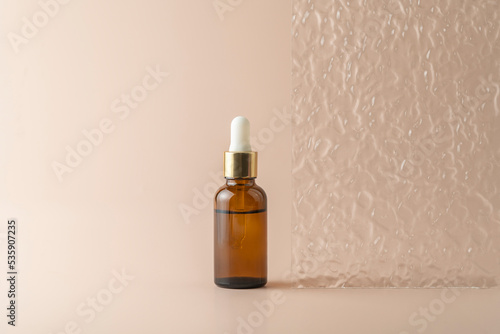 A face serum or essential oil in a brown dropper bottle standing on a beige background