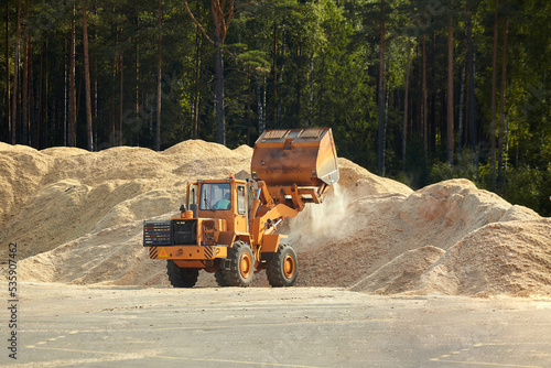 working bulldozer unloads against the background of large mountains of small wooden sawdust
