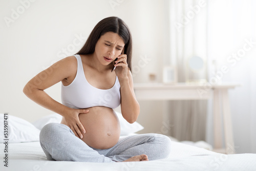 Upset pregnant woman feeling some pain and discomfort, calling doctor photo