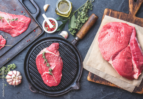 Fresh raw meat. Beef Tenderloin and marbled beef steaks on grill pan and frying board with seasoning, black background top view photo