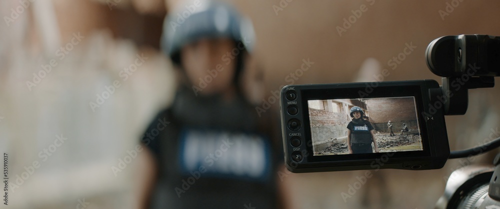 POV Camera view, female war journalist correspondent wearing bulletproof vest and helmet reporting live near destroyed building POV Camera view, female war journalist correspondent wearing bulletproof vest and helmet reporting live near destroyed building