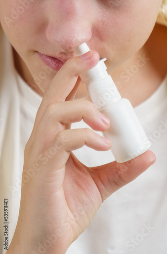 A girl with a cold treats a runny nose with a nasal spray.