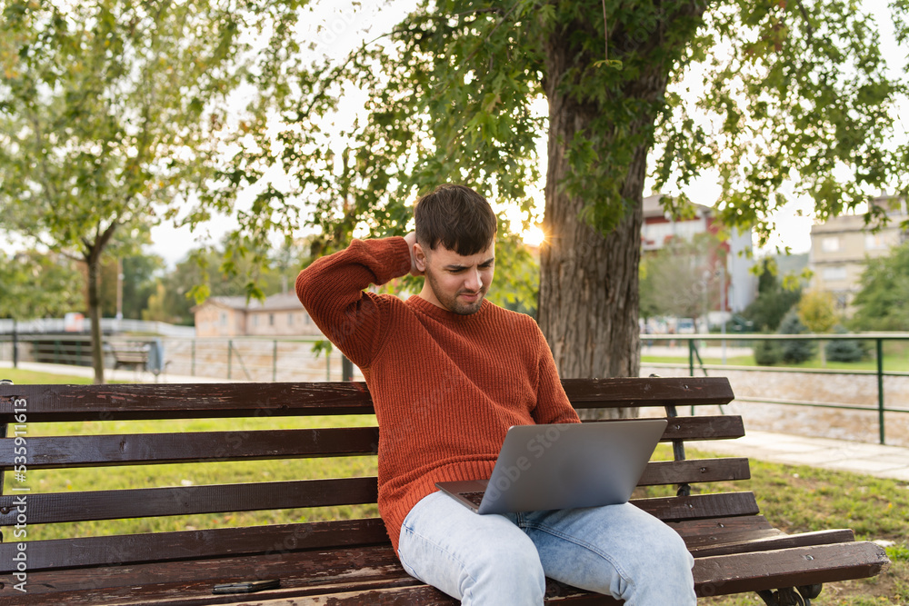 A young businessman outdoors in park sitting with his laptop talking on phone enjoying outside A young businessman outdoors in park sitting with his laptop talking on phone enjoying outside