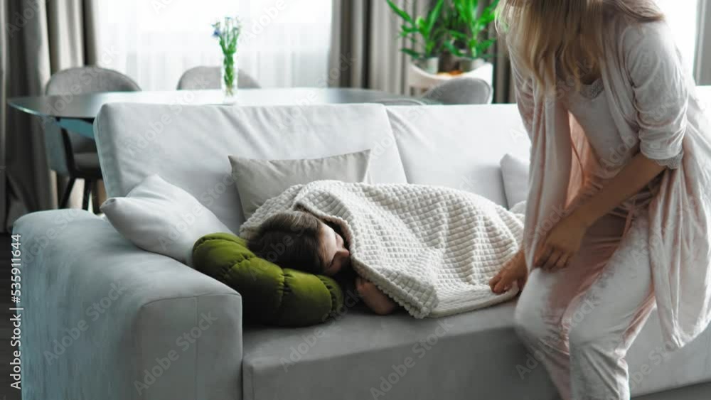 Child kid girl is going to sleep lying on the sofa and mother covering ...