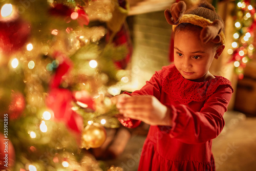 Magical portrait of cute little girl decorating Christmas tree with twinkling lights, copy space