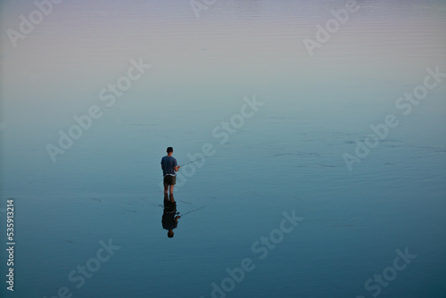 A fisherman stands in the water and catches fish with a fishing rod. River or lake, no waves