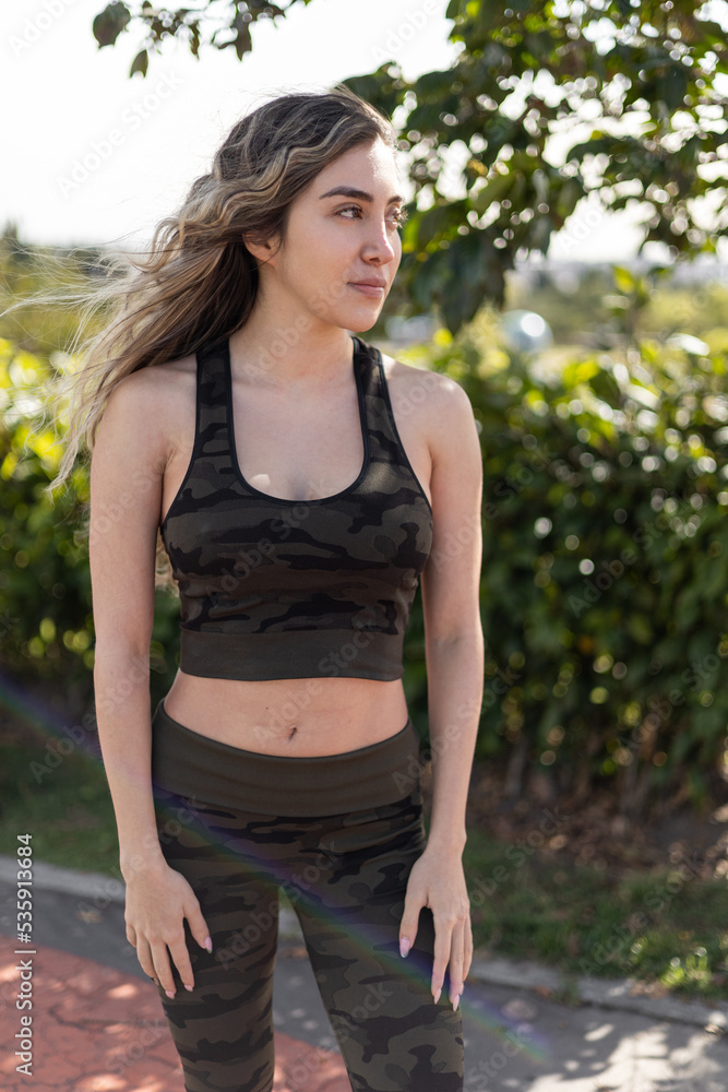 sunny day wearing sportswear a young woman with long hair, posing standing in a park, lifestyle sunny day wearing sportswear a young woman with long hair, posing standing in a park, lifestyle