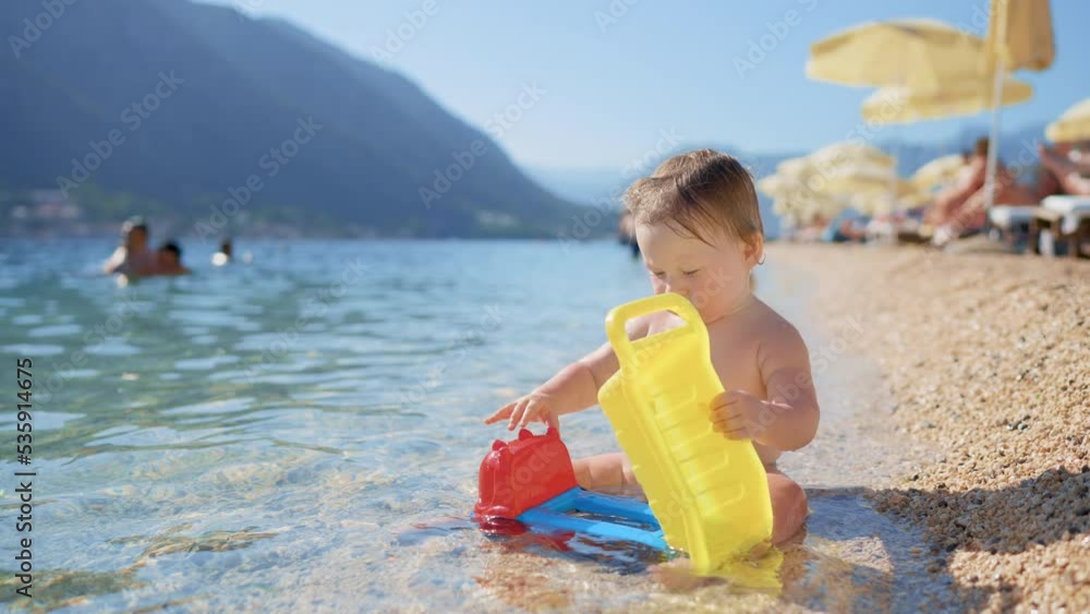 Little blonde asian baby boy playing with stones beach ocean sea. Child building stone castle house. Family summer holidays and trips to warm countries. Happy tourism vacation clean blue waves water Little blonde asian baby boy playing with stones beach ocean sea. Child building stone castle house. Family summer holidays and trips to warm countries. Happy tourism vacation clean blue waves water